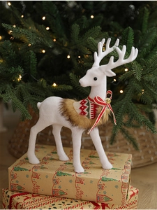 Detailed view of a white flocked reindeer statue on gift boxes with festive Christmas tree background