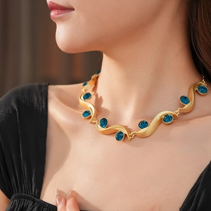 Close-up of a vintage golden wavy necklace with inlaid blue gemstones worn by a model