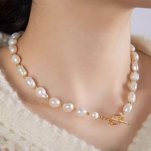 Close-up of white baroque pearl necklace with gold beads and toggle clasp on neck