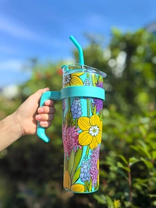Detail of 40oz insulated tumbler with floral pattern and turquoise handle held outdoors