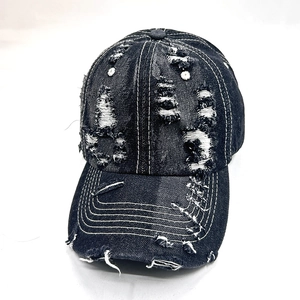 Close-up of black distressed denim baseball cap with ripped details and white stitching