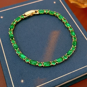 Detail of emerald green rectangular cut stones on a gold plated tennis bracelet