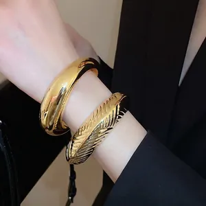 Bracelet jonc ouvert ovale épais avec rayures dorées porté au poignet d'un mannequin