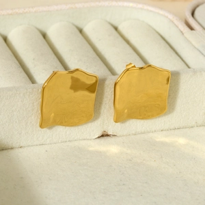 Dettaglio degli orecchini geometrici dorati irregolari su superficie in velluto beige