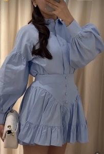 Detail of light blue dress with puffy sleeves, buttoned waist belt, and ruffled skirt hem