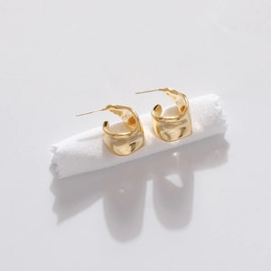 Minimalist gold geometric hoop earrings with polished metallic finish on white fabric