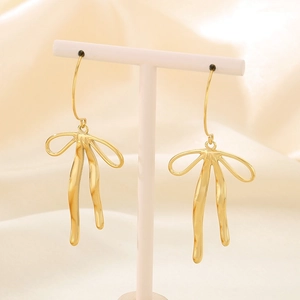 Close-up of elegant gold bow-shaped drop earrings on soft beige silk background
