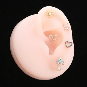 Macro shot of various heart and star stud earrings displayed on a silicone ear model
