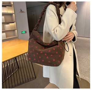 Detail of brown corduroy shoulder bag with strawberry print and ruched strap on a model