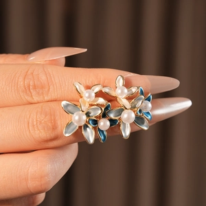 Macro view of flower stud earring with blue enamel petals and a central pearl accent