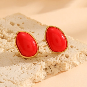 Dettaglio di orecchini ovali dorati con pietre rosse su sfondo di pietra beige