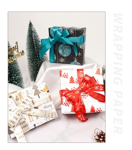 Three Christmas wrapping paper rolls with festive motifs, ribbons, and gift boxes setup
