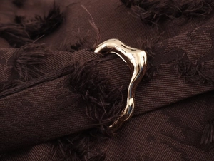 Makro-Detail einer glänzenden goldenen Metallschnalle auf strukturiertem braunem Jacquard