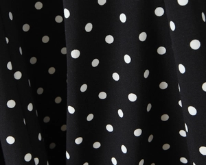 Gros plan sur tissu noir à pois blancs montrant la texture fine et le drapé souple