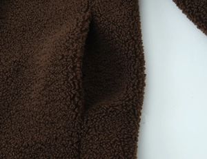 Close-up of the deep brown faux shearling fabric texture and side pocket detail on the long coat
