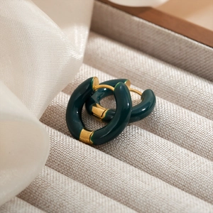Macro detail of dark green enamel hoop earrings with gold metal accents on silk