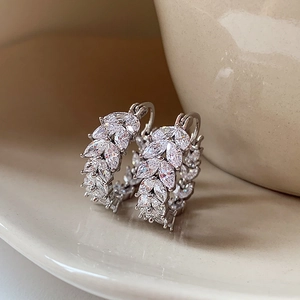 Dettaglio di orecchini a foglia d'argento con zirconi lucidi su un vassoio ceramico