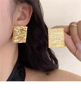 Close-up of golden square stud earrings with unique hammered pleated texture on ear