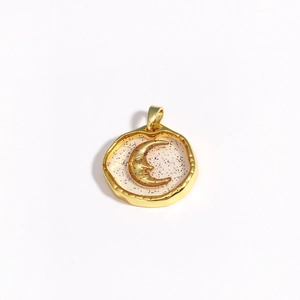 Close-up of a round gold moon pendant featuring purple glitter and irregular gold frame