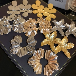 Macro view of oversized fan-shaped floral metal earrings with smooth gold and silver finish