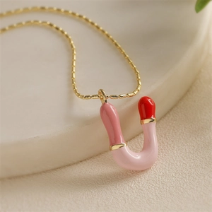 Gros plan d'un pendentif en U doré avec émail rose et rouge sur une chaîne à maillons fine