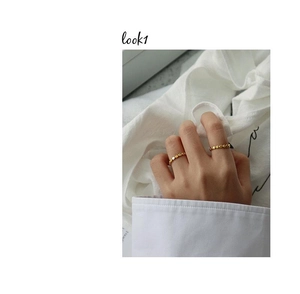 Close-up of two minimalist gold beaded silver rings worn on model against white fabric
