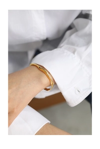 Detailed view of an irregular wavy gold bracelet on a wrist with a white shirt