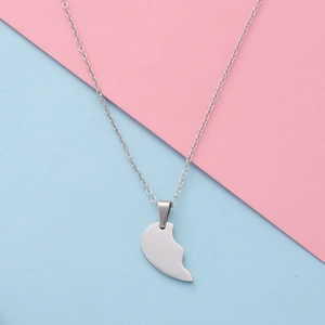 Polished silver half-heart pendant necklace displayed on a pastel blue and pink surface