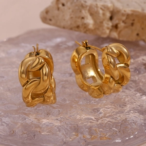 Detail of chunky gold chain link earrings on a textured glass surface with natural stone