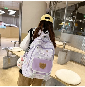 Close-up of a purple plaid backpack featuring bear embroidery and a white rabbit charm