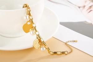Détail de breloques cœur et pièce dorées avec perles sur bracelet acier inoxydable