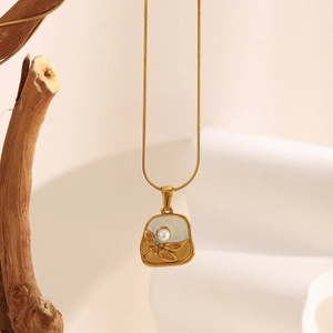 Detail of 18K gold plated dragonfly and pearl flower pendant on a square enamel base