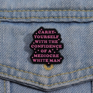 Pink enamel badge with confidence quote pinned on denim jacket pocket