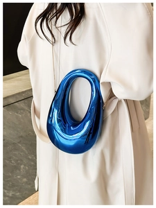 Blue metallic fluid-shaped crossbody bag with a high-gloss finish on a white coat