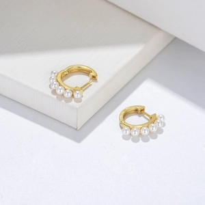 Classic gold S925 silver hoop earrings with small white pearls on textured background