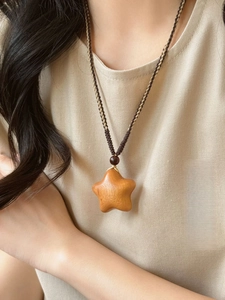 Detail of wooden star pendant with hand-woven rope necklace on beige fabric background