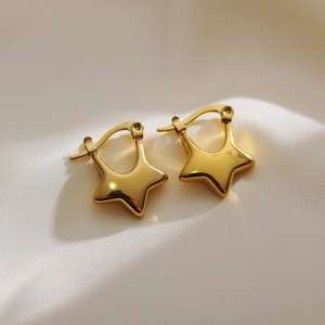 Polished gold plated stainless steel star hoop earrings on white satin fabric background