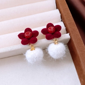 Close-up of red flocked flower earrings with soft white pompom pendants and gold links