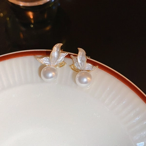 Macro shot of elegant butterfly earrings with white pearls hanging on a white porcelain dish