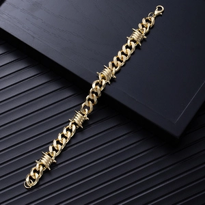 Detailed close-up of golden metal cuban chain with thorn wire charms on a dark tray