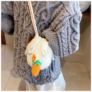Detail of hand-knitted bucket bag featuring a 3D carrot motif and woven shoulder strap