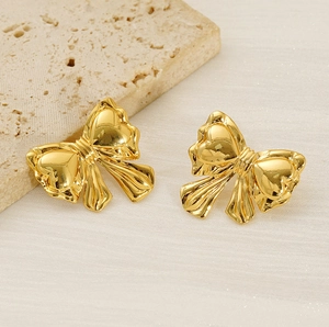 Detailed macro view of golden bow earrings featuring a polished mirror-like metallic finish