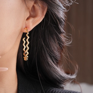 Close-up of a model wearing a wavy C-shaped gold-plated earring with a glossy finish