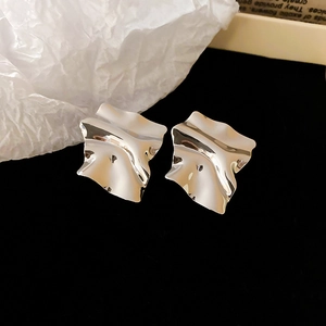 Macro shot of silver plated irregular wavy square studs on black velvet background