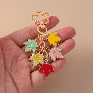 Close-up of golden enamel keychain with five colorful maple leaf charms held in hand