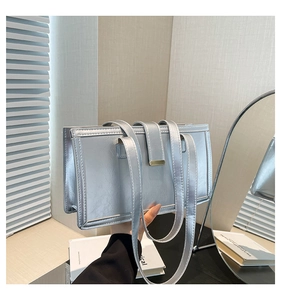 Detail of a silver rectangular handbag with double straps held in a cozy indoor setting