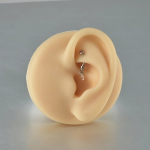 Macro detail of G23 titanium ear piercing with pink heart zircon pendant on ear model