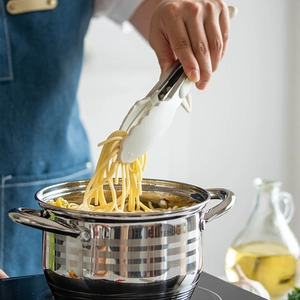 White heat-resistant silicone food tongs with stand picking up pasta from a cooking pot