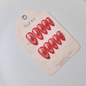 Detail of red cherry almond press-on nails with 3D gems on a marble display card