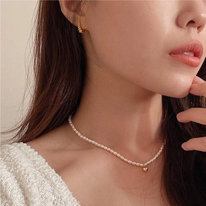 Detail of cream white mini pearl necklace with gold heart pendant worn by model